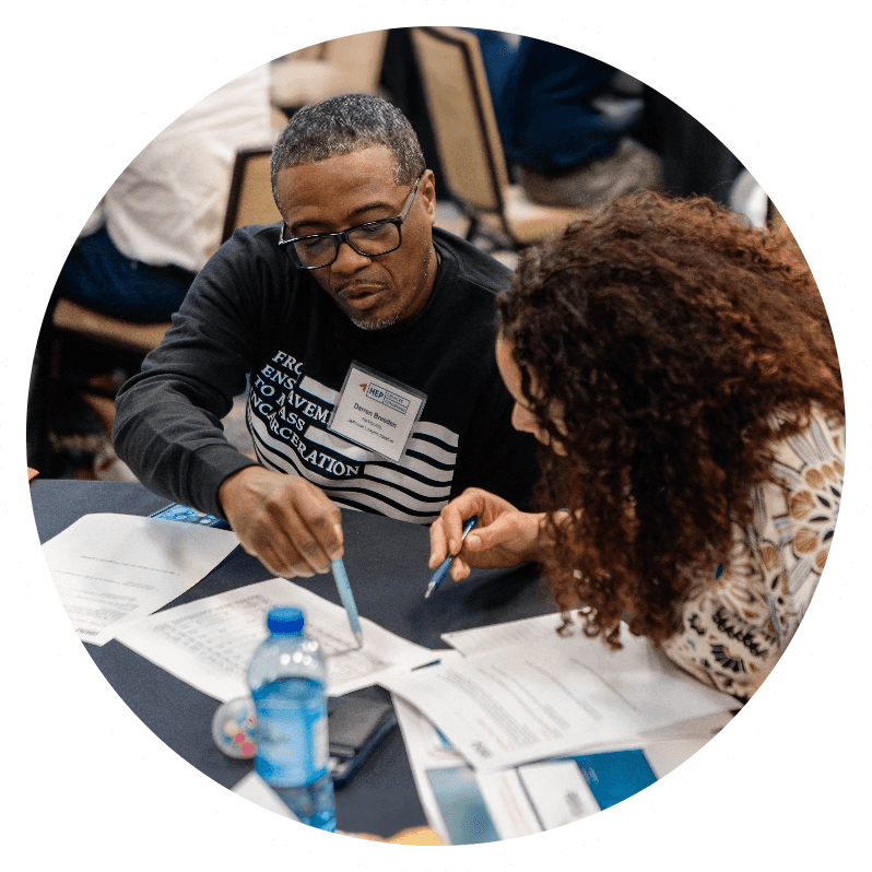A man in glasses and a woman point attentively at paperwork on a table, having a discussion about it.