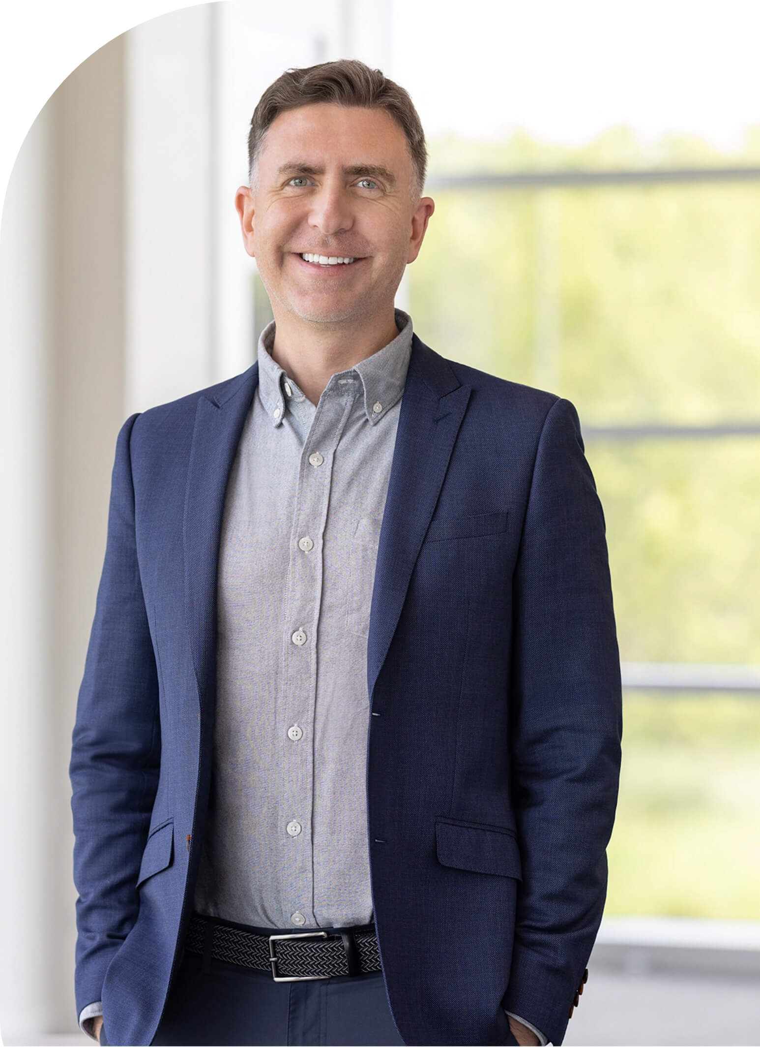 A photo of Keith Witham standing in a blue suit and smiling in front of sunny windows.